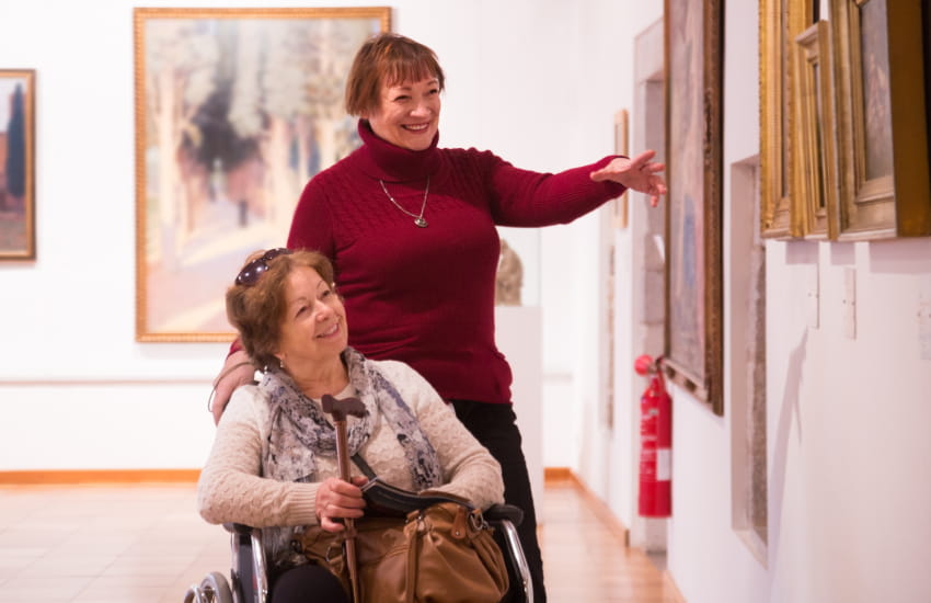 two women, one standing and one in a wheelchair, tour an art exhibit in a museum