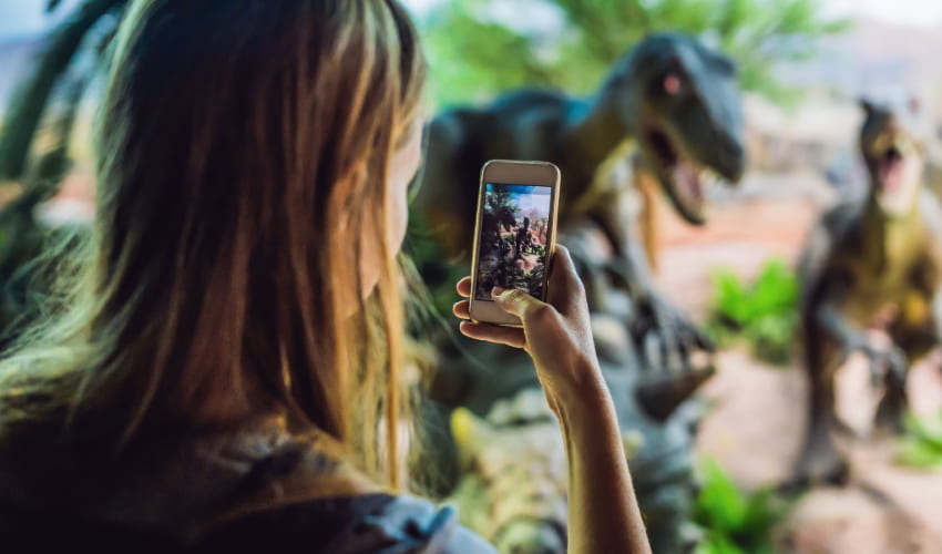 a woman used her smart phone to take a picture of dinosaur models in a science museum