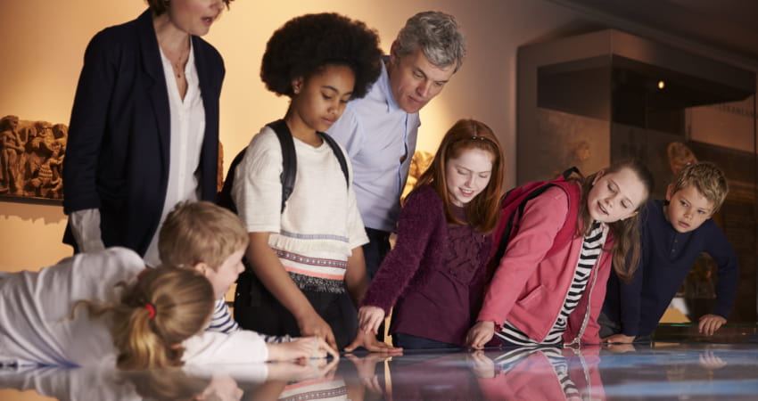 a group of students and chaperones gather around a display at a history museum