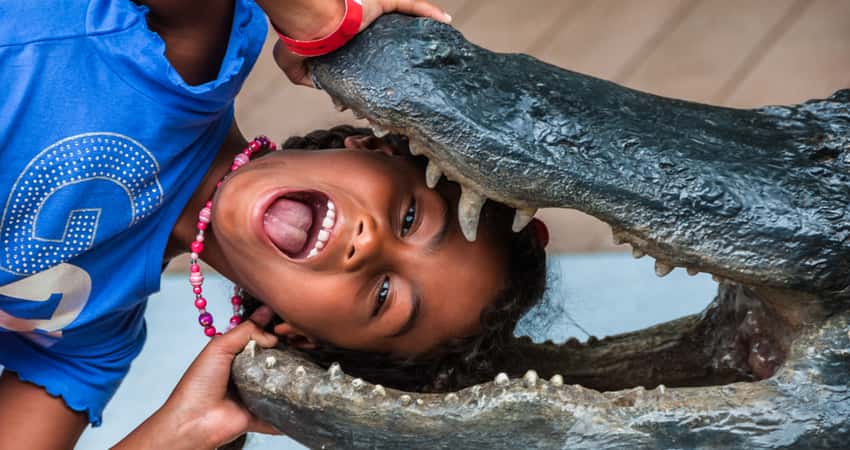 A little girl taking a photo in the mouth of a alligator sculpture