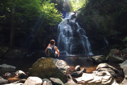 A hiker sits on a rock near a waterfall in the Great Smoky Mountains