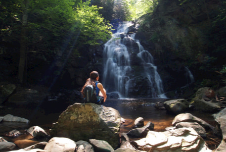 A hiker sits on a rock near a waterfall in the Great Smoky Mountains