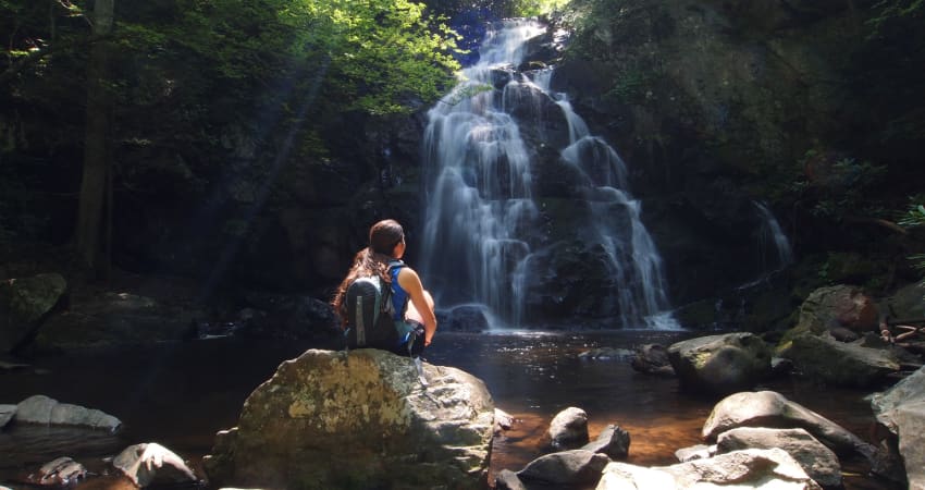 A hiker sits on a rock near a waterfall in the Great Smoky Mountains