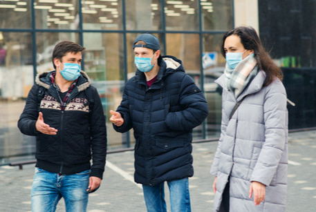 A group of people wearing masks talking on the sidewalk