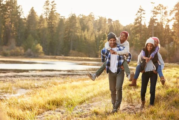 Two parents carrying kids piggyback past fall trees