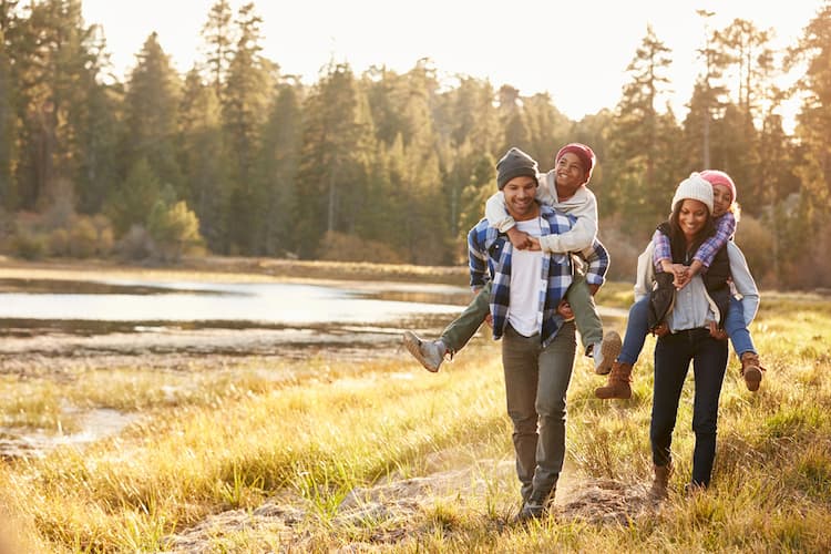 Two parents carrying kids piggyback past fall trees