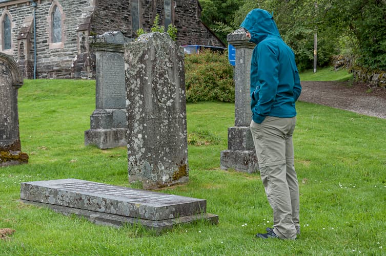 Man in blue jacket standing by grave