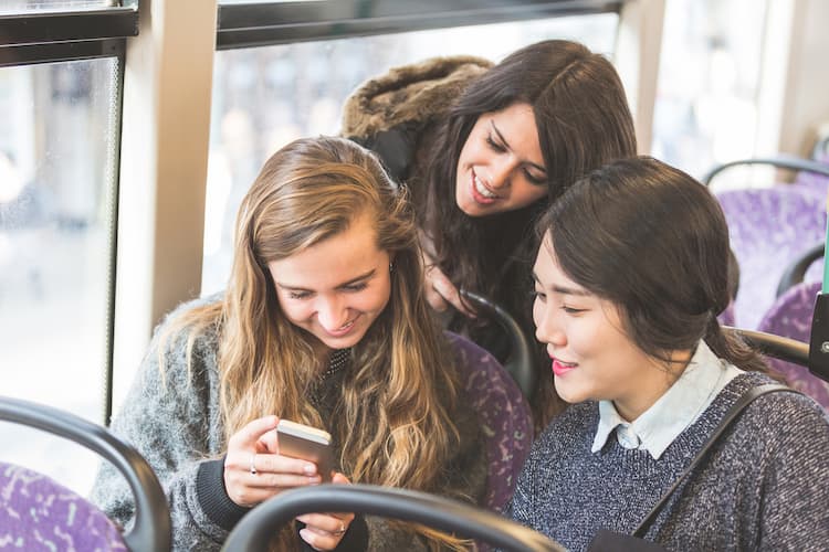 Three young women looking at phone on bus