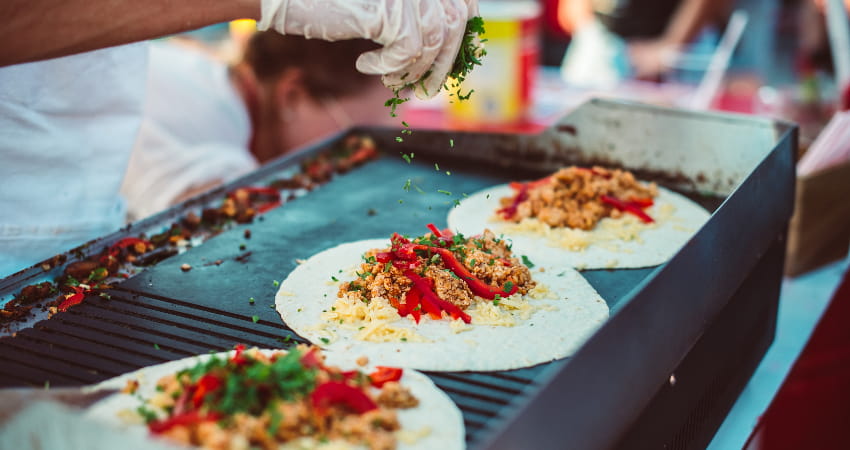 A chef heats up tortillas filled with toppings on a flat-top grill