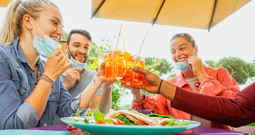 A group of friends toasting drinks over lunch under a patio umbrella