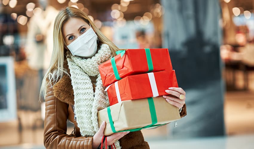 A woman wears a mask and holds a stack of wrapped holiday gifts