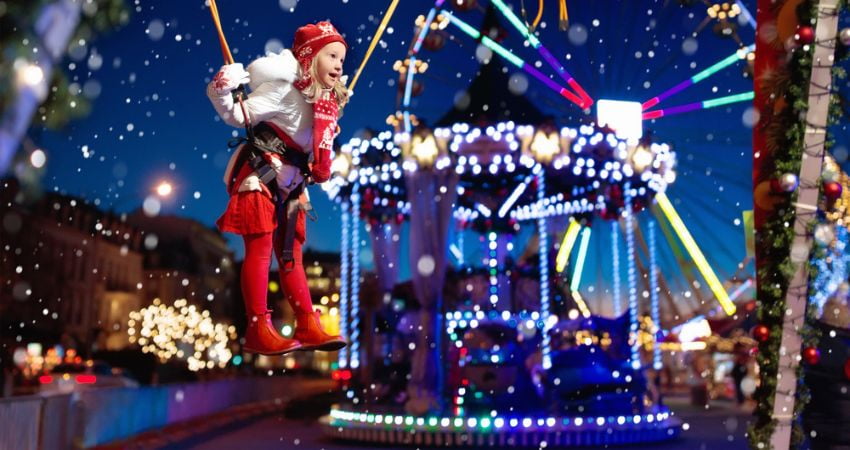 little girl on a swing with amusement park lights in the background