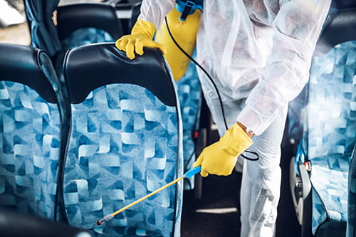 A person in protective clothing sanitizes a bus seat