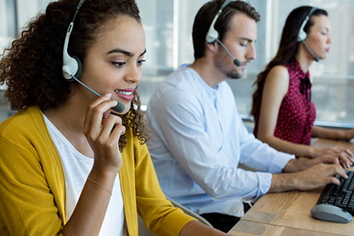 A lineup of customer support agents answer phones via headsets
