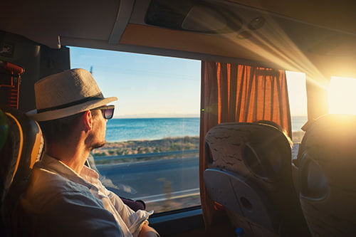 A passenger looks at a beach out the window of a moving charter bus