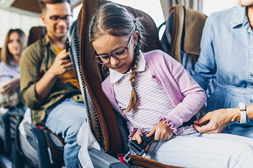 A child on a charter bus buckles her seatbelt